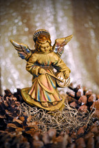 Figurine of an angel seated on the rocks playing a drum; a Christmas decoration set among pine cones and Spanish moss.