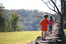 children walking on the top of a stone wall outdoors 