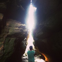 Man standing in sunlight beaming through cavern between two rocks.