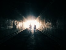 two men walking towards light at the end of a tunnel 