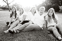 Five women sitting together on a grassy lawn.