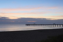 Long pier off beach in ocean at dusk.