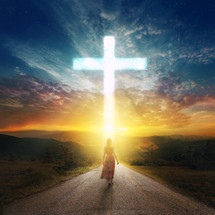 woman walking down a road towards a cross in the sky