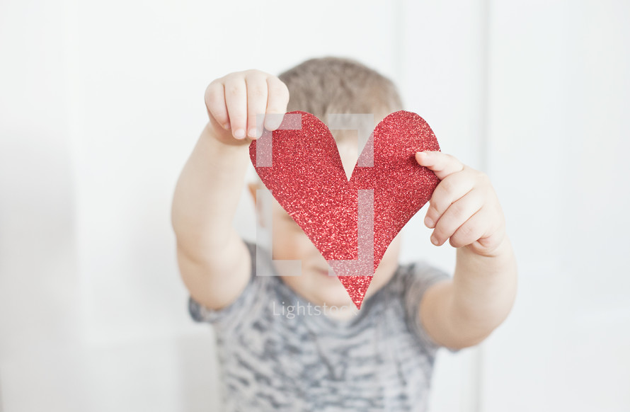 Toddler child holding red paper heart cut out in front of face.