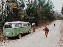 A man and two children near a green van on a country road.
