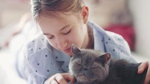 Girl strokes a grey cat while reading a book. Cute white cat lies next to a child reading a book and taking time to a pet. 