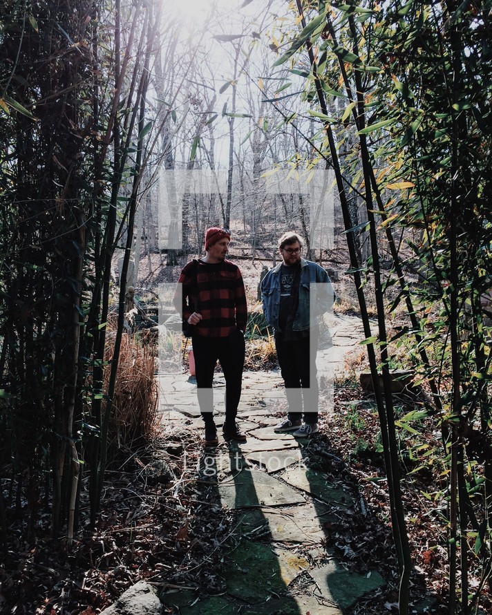 two men standing on a path surrounded by bamboo