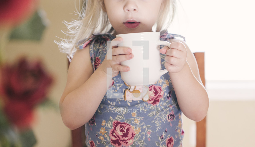 a toddler girl holding a mug 