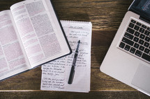 open Bible and notes on a notepad and pen and laptop 