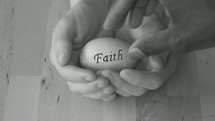 cupped hands holding an egg with the faith hope on it 