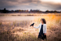 a child in a field holding a crow in her hand 