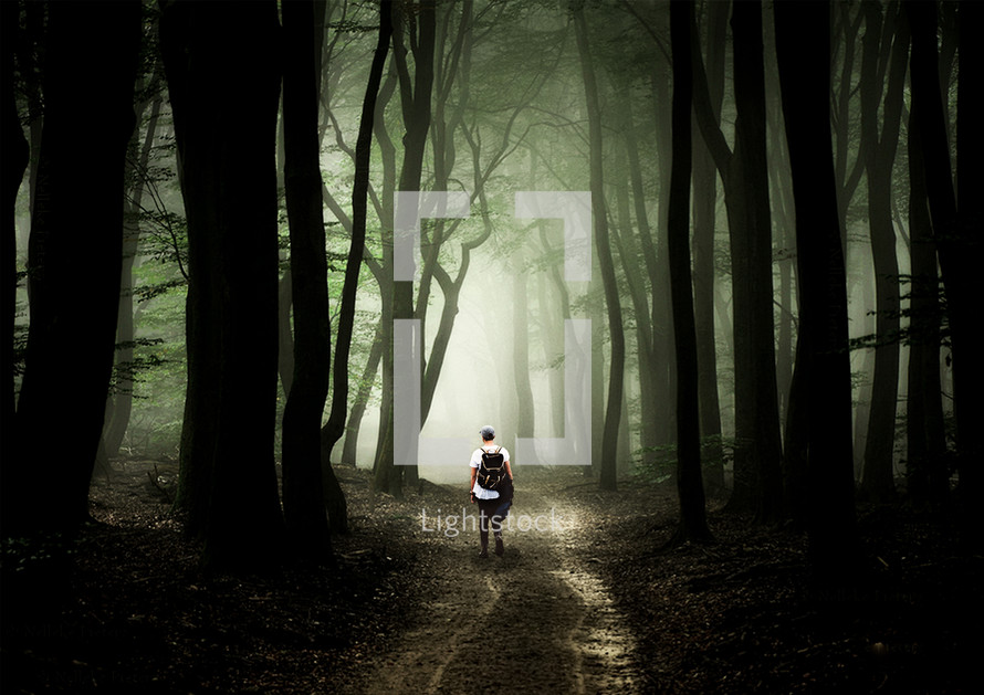 a man walking on a dirt road through a forest 