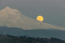 super moon behind a snow capped mountain peak 