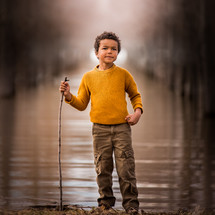 a child standing beside a pond holding a stick 
