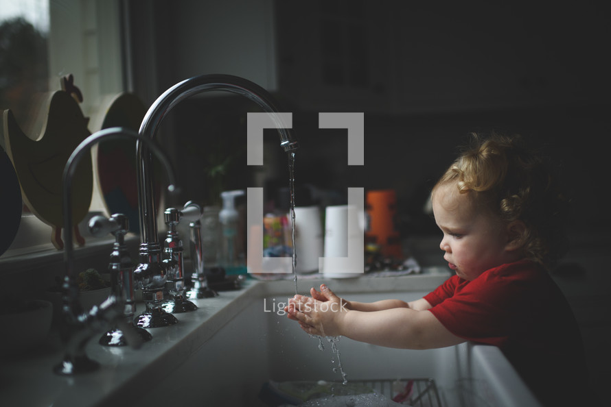 toddler girl playing in water at the kitchen sink 