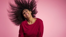 Beautiful african american woman with afro hair having fun smiling and dancing in studio against pink background. slow motion.