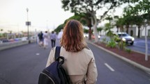 Unrecognizable woman walks along busy city street with backpack on shoulder. Female student returns after classes from university. Lady tourist walking alone in Europe. High quality 4k footage