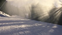 Skier skiing trough misty clouds of fresh snow from snow cannon in winter ski resort, holiday sports recreation

