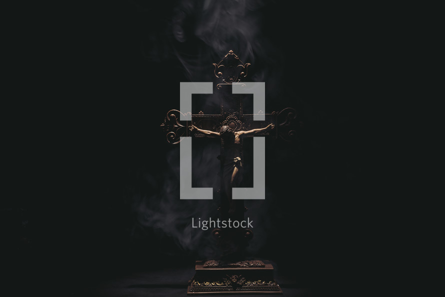 Dark and moody Jesus on a wooden cross with smoke and dramatic lighting.