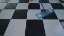 Close up of mop cleaning a black and white floor.