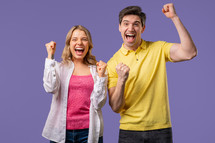 Pretty woman and man shows triumph yes gesture of victory, achieved result, goals. Stylish couple glad, happy, surprised excited on violet background. Jackpot concept. High quality 