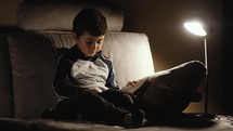 a little boy sitting on a couch reading a Bible 