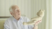 Senior caucasian man holding old teddy bear themes of reminiscing memories childhood nostalgia