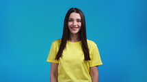 Beautiful woman looking to camera and smiling. Beautiful model girl in yellow t-shirt on blue studio background. High quality 4k footage