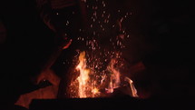 Sparks and embers fly up as wood in stoked in bonfire.