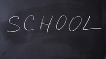 Bold white chalk letters spell School. Inscription SCHOOL. Chalk writing on blackboard. Concept of beginning of school year.	