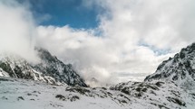 Clouds roll in snowy mountains valley with chamois looking for food in winter time lapse
