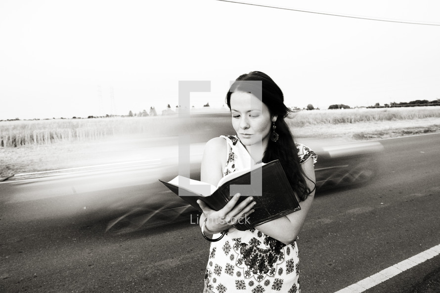 woman reading a Bible in front of speeding cars on a highway