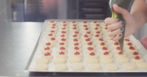 Baker piping strawberry jam onto a sheet of cookies.