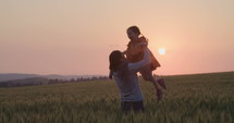 Mother and young daughter in a wheat field during sunset.