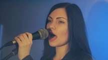 Close-up of the face of the singer with microphone on a lit stage lighting and smoky background. Singer sings a song on stage in concert lighting