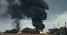 Accident in oil refinery - huge explosions and fireballs rising while thick black smoke covers the sky.