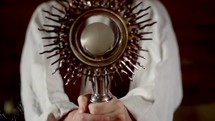 Priest holding a monstrance and blessing a Bible with the sign of the cross.