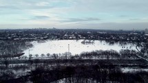 Drone shot of Riverdale Park East in dynamic urban view of Toronto city on a winter day. Aircraft flying right above highway while people playing with snow in the distance. Drone moving forward.