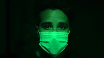 man standing in green light wearing a surgical mask 