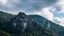 Dramatic clouds moving over green forest mountains and rocky tower Time lapse
