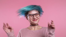 Unusual woman with blue hair having fun, smiling, dancing with head in studio against pink background. Music, dance concept, slow motion