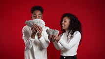 Satisfied happy excited african american couple showing money - USD currency dollars banknotes on red wall. Symbol of success, gain, victory. Slow motion.