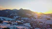Aerial panoramic view of beautiful sunset over small village in winter alpine mountains nature
