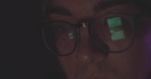 Close up of young man's face as he scrolls on phone in a dark room