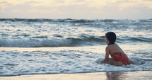 Little girl playing on the beach in the water during sunset hour