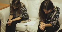 Two women praying on a couch