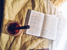 an open Bible on a bed and spoon in a jar 