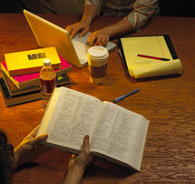 Two women at a table with Bible, computer, notebook, books and coffee.