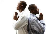 Two men standing back to back with praying hands.