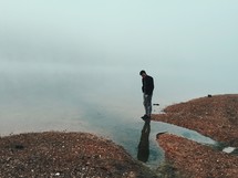 a man standing looking down at water in a lake